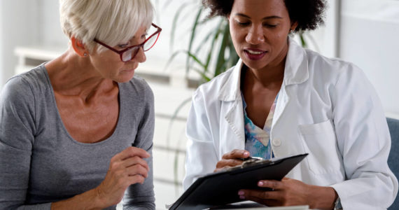 A female doctor sits at her desk and chats to an elderly female patient while looking at her  test results