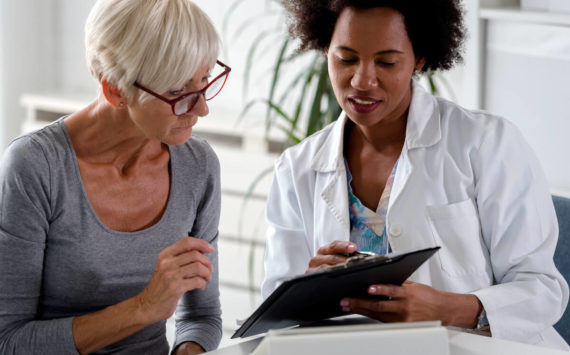 A female doctor sits at her desk and chats to an elderly female patient while looking at her  test results