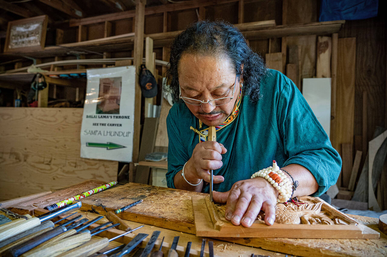 (Photo by David Welton) Sampa Lhundup works on a carving of a Tibetan bird in his studio. A sign in the background proudly proclaims him as the carver of the Dalai Lama’s teaching throne.